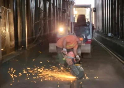 construction workers in helmets and vests are cleaning a dusty tunnel with stacks of wood visible in the background.