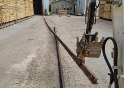 A construction site with stacked lumber, a rail track curving towards a building, and equipment reaching for the track.